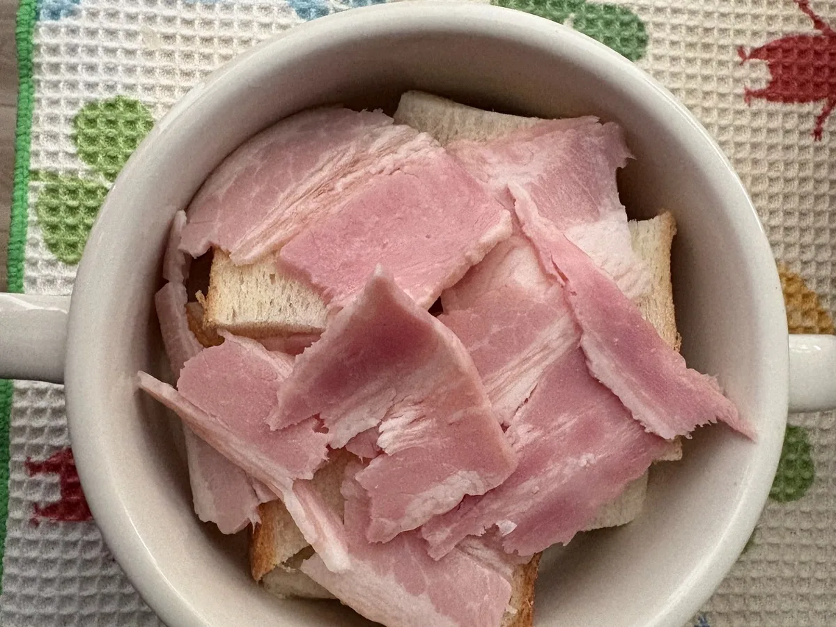 マグカップに詰めた食パンの上に、手でちぎったベーコンをのせたところ